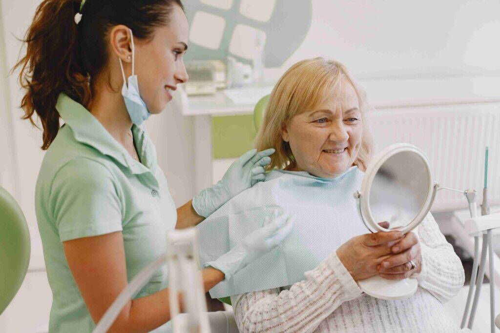 Senior patient smiling with mirror after treatment.